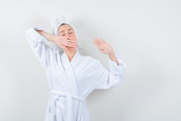 young-woman-stretching-upper-body-while-yawning-white-bathrobe-towel-looking-relaxed-front-view_176474-50741